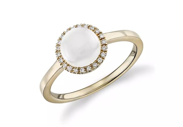 A white moonstone cabochon ring with diamond halo in yellow gold